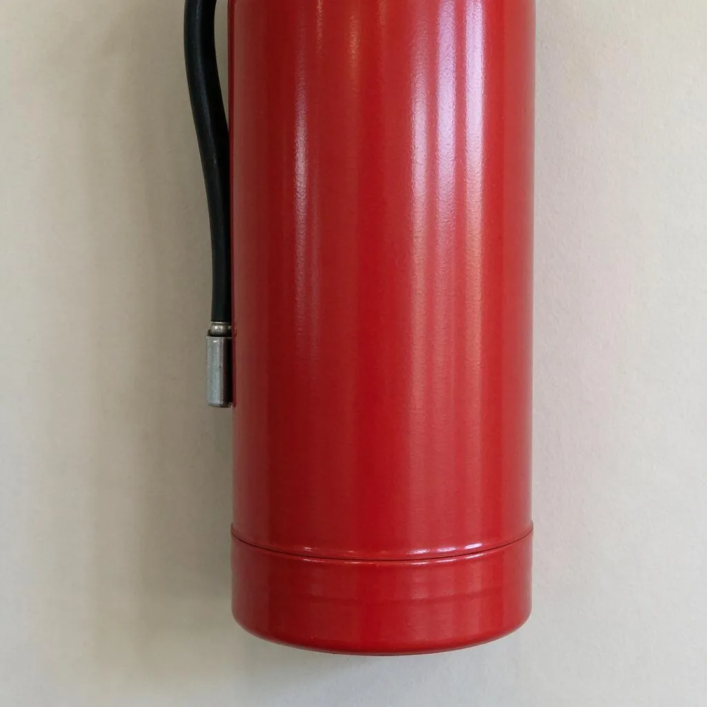 Illustration d’un extincteur rouge suspendu à un mur clair uni